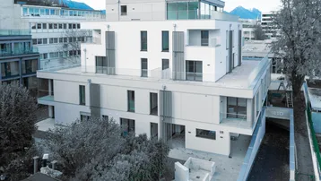 Moderne Wohnanlage mit weißer Fassade, großen Fenstern und Balkonen in städtischer Umgebung.