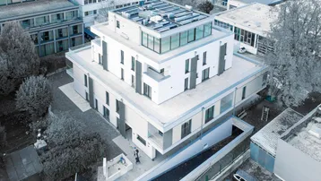 Moderne Wohnanlage mit Flachdach und Photovoltaikanlage in städtischer Umgebung.