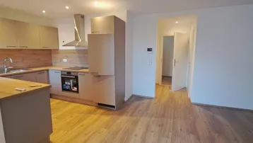 Moderne Einbauküche mit Holzoptik-Arbeitsplatten und hellem Laminatboden in einem offenen Wohnbereich.