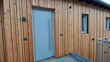 Moderne Eingangstür mit Holzfassade und schlichten Wandleuchten, die einladend wirken.