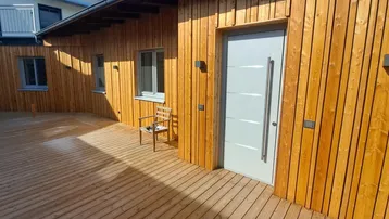 Große Holzterrasse mit moderner Eingangstür und Holzfassade, ideal für entspannte Stunden im Freien.