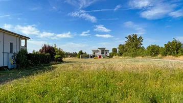 Weitläufiges Grundstück mit grüner Wiese und moderner Architektur im Hintergrund unter blauem Himmel.
