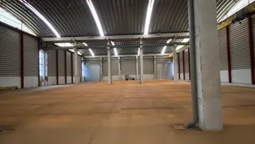 Große, leere Lagerhalle mit gewölbtem Dach und natürlichem Lichteinfall durch Dachfenster.