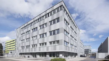 Modernes Bürogebäude mit gestreifter Fassade und vielen Fenstern unter blauem Himmel.