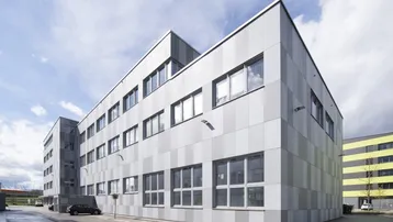 Modernes Bürogebäude mit gestreifter Fassade und großen Fenstern unter bewölktem Himmel.
