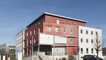 Modernes Bürogebäude mit roter und weißer Fassade unter blauem Himmel und Parkplätzen.