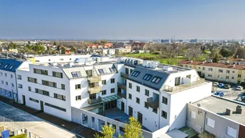 Luftaufnahme eines modernen weißen Wohnkomplexes mit Innenhof und umliegender Stadtlandschaft.