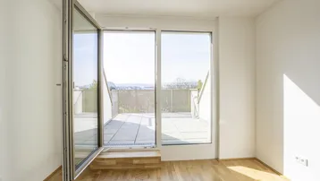 Helles Zimmer mit Holzboden und Zugang zu einer großen Terrasse mit Weitblick.