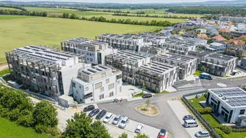 Luftaufnahme einer modernen Wohnanlage mit mehreren Gebäuden, umgeben von grünen Feldern und ländlicher Landschaft.