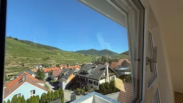 Panoramablick aus dem Fenster auf ein malerisches Dorf und weitläufige Weinberge unter blauem Himmel.