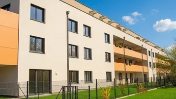 Moderne Wohnanlage mit hellen Fassaden, orangefarbenen Balkonen und gepflegter Grünfläche im Vordergrund.