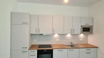 Moderne Einbauküche mit hellgrauen Schränken, Holz-Arbeitsplatten und integrierten Geräten.
