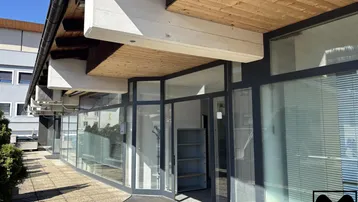 Eingangsbereich eines Geschäftsgebäudes mit großen Glasfronten und Holzverkleidung unter dem Vordach.