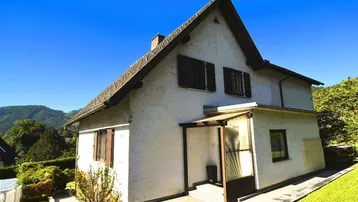 Charmantes Einfamilienhaus mit Satteldach und grüner Umgebung unter blauem Himmel.