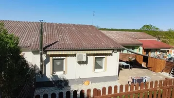 Rückseite eines Hauses mit kleiner Terrasse, Gartenmöbeln und Blick ins Grüne.