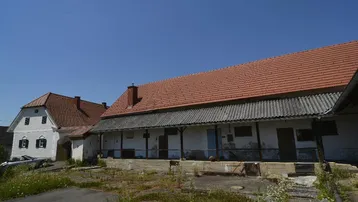 Ländliches Anwesen mit mehreren Gebäuden und traditionellen Ziegeldächern unter blauem Himmel.