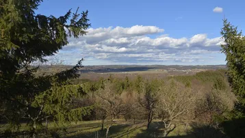 Weitläufiger Panoramablick über ein Tal und bewaldete Hügel unter einem strahlend blauen Himmel.