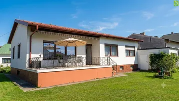 Einfamilienhaus mit großer Terrasse, Garten und Markise unter blauem Himmel.