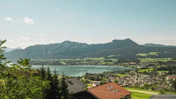 Panoramablick über eine malerische Seenlandschaft mit umliegenden Bergen und Siedlungen.