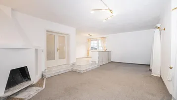 Geräumiges Wohnzimmer mit Kamin, Teppichboden und einem erhöhten Bereich mit Fliesen.