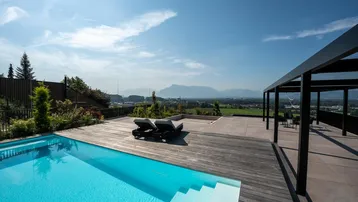 Große Sonnenterrasse mit modernem Pool, Liegestühlen und weitem Bergblick unter blauem Himmel.