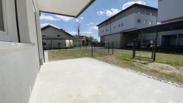 Große geflieste Terrasse mit Kiesstreifen und Blick auf die umliegenden Gebäude und Carports.