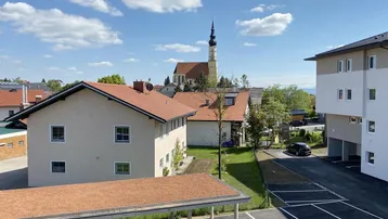 Blick auf die Wohnanlage mit Parkplätzen, Carports und einer Kirche im Hintergrund unter blauem Himmel.