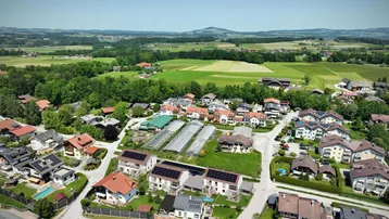 Weitläufige Luftaufnahme einer Wohnsiedlung mit vielen Häusern, umgeben von grünen Feldern und Hügeln.