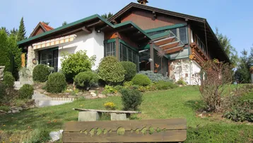 Charmantes Landhaus mit Holzfassade und gepflegtem Garten auf einem Hanggrundstück.