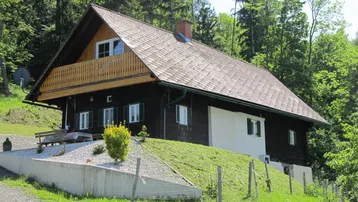 Charmantes Landhaus mit Holzbalkon und Satteldach, eingebettet in eine grüne Hügellandschaft.