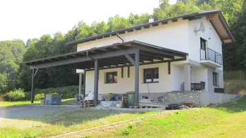 Modernes Einfamilienhaus mit weißer Fassade, Carport und umgebender Natur.