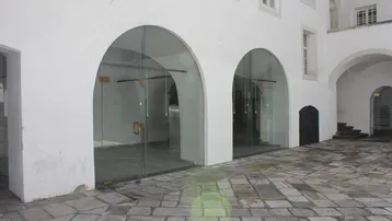Historischer Innenhof mit Steinpflaster und großen Bogenöffnungen, die zu Geschäftsräumen führen.