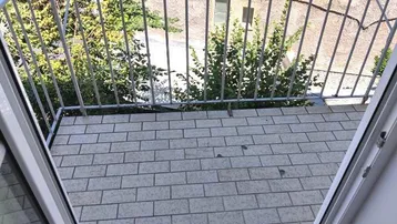 Kleiner Balkon mit Fliesenboden und Blick auf den begrünten Innenhof.