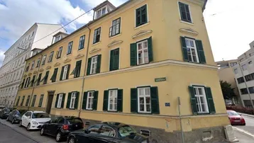 Historisches Gebäude mit gelber Fassade und grünen Fensterläden an einer städtischen Straße.