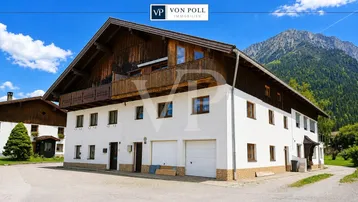 Traditionelles Alpenhaus mit Holzbalkon und beeindruckendem Bergblick unter blauem Himmel.