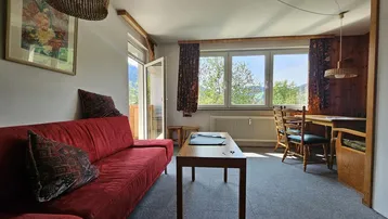 Gemütlicher Wohn- und Essbereich mit rotem Sofa, Holztäfelung und Blick auf die Berge.