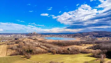 Weitläufige Landschaft mit einem See und einer Burg in der Ferne unter blauem Himmel.