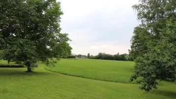 Weitläufige grüne Landschaft mit Bäumen unter bewölktem Himmel, die eine ruhige Umgebung zeigt.