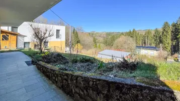 Gepflasterter Außenbereich mit Steinmauer und weitem Blick auf die bewaldete Landschaft.