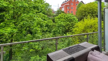 Balkon mit Blick ins Grüne und auf ein rotes Gebäude in der Ferne.