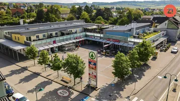 Luftaufnahme eines modernen Geschäftskomplexes mit Wohnungen, zentralem Platz und grüner Umgebung.