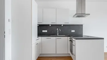 Moderne, weiße Einbauküche mit dunkler Arbeitsplatte und Holzboden in neuwertigem Zustand.