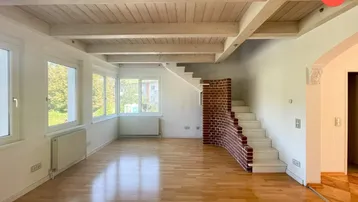 Helles Wohnzimmer mit Holzbalkendecke, Parkettboden und einer markanten Ziegelstein-Treppe.
