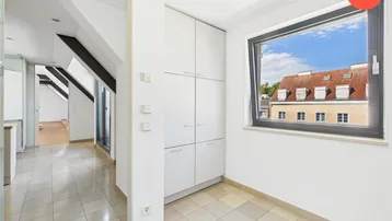 Heller Flur mit Fliesenboden, Einbauschränken und Fenster mit Blick auf Dächer.