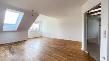 Helles Zimmer mit Holzboden und Dachschrägenfenstern, ideal als Wohn- oder Schlafbereich.