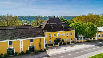 Luftaufnahme eines traditionellen gelben Gebäudekomplexes mit dunklen Dächern und umgebender Natur.