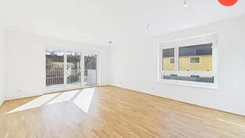Helles Wohnzimmer mit Parkettboden, großen Fenstern und Zugang zu einem Balkon.