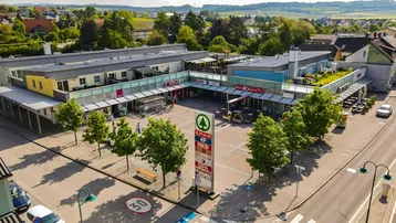 Luftaufnahme eines modernen Geschäfts- und Wohnkomplexes mit Flachdächern und begrünten Terrassen in ländlicher Umgebung.