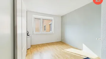 Helles Schlafzimmer mit Parkettboden, einer hellgrauen Akzentwand und Fenster.