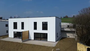 Moderner Neubau mit weißer Fassade, großen Fenstern und einer kleinen Terrasse im Bau.